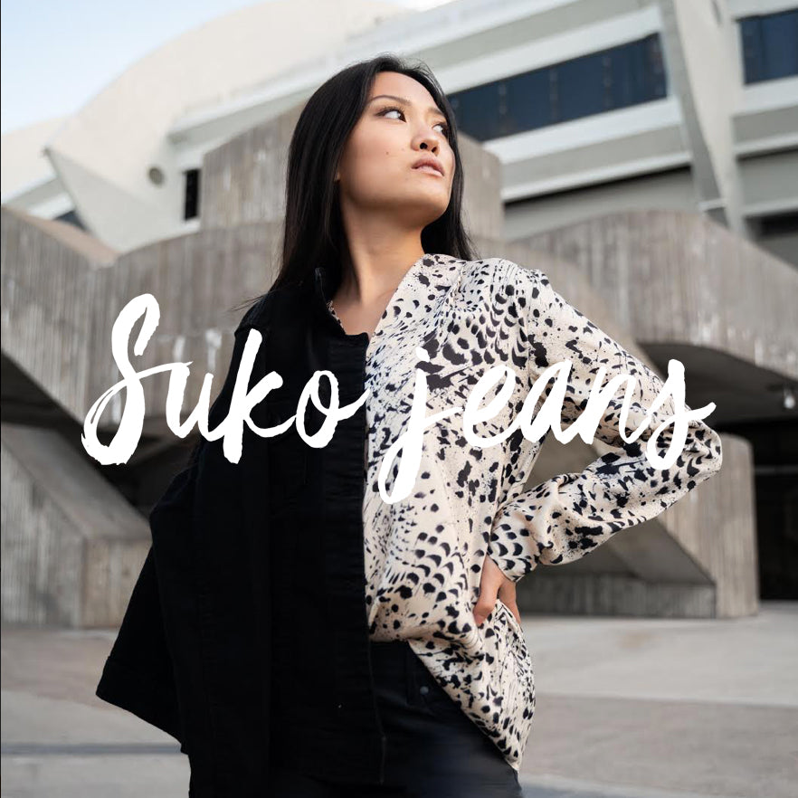 Click here to see Suko Jeans Product - Picture of a A young woman standing confidently over a grey building